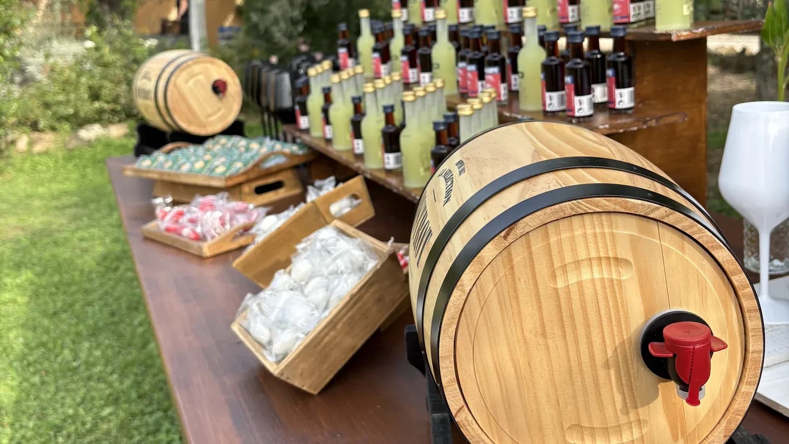The Italian Market favour table at a wedding in Tuscany: olive-oil barrels, bottles and sweets laid out under the olive trees