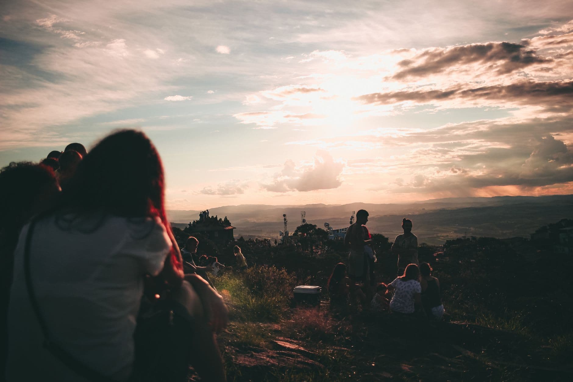 Silhouette of a group of friends relaxing on a hill overlooking a scenic sunset.