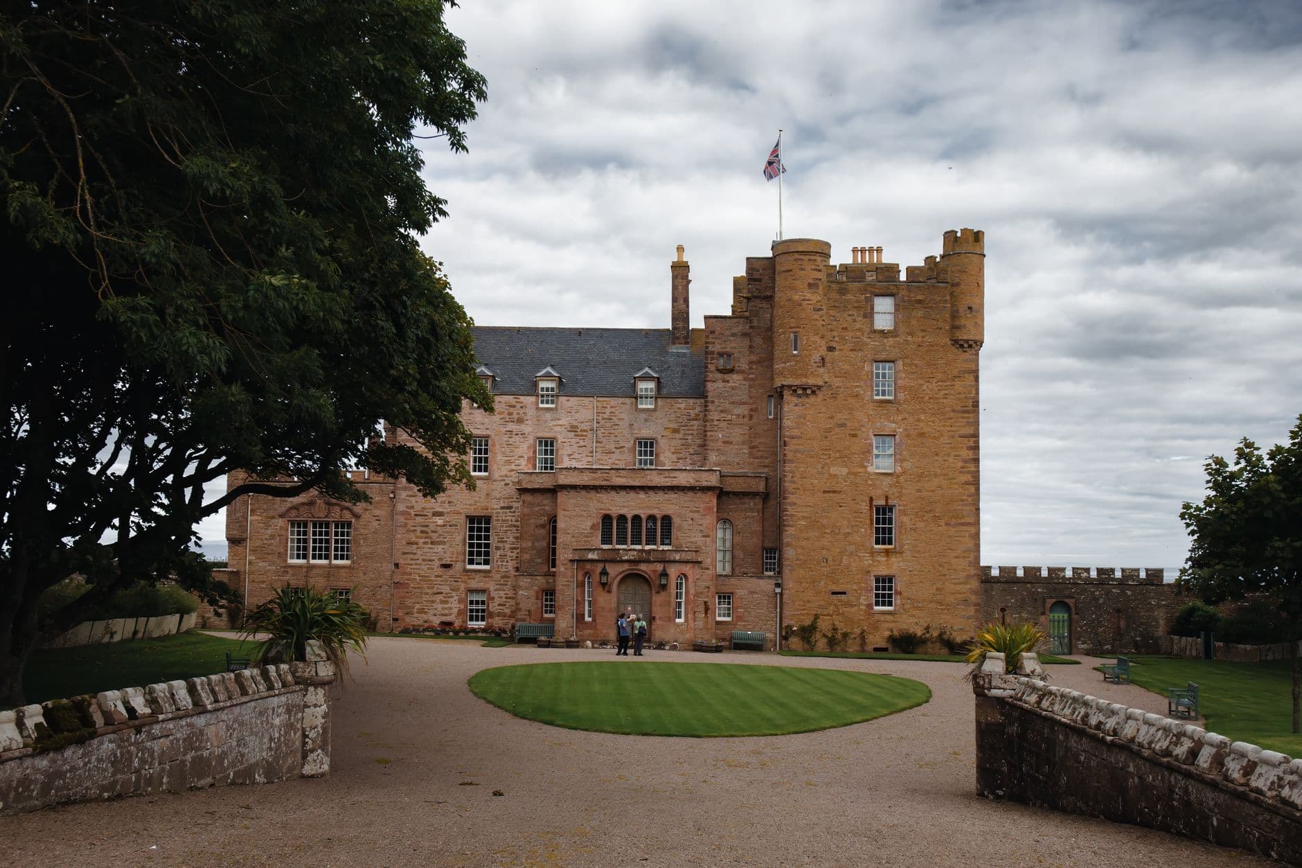 View of the historic Castle of Mey in Scotland, surrounded by lush gardens and a cloudy sky.
