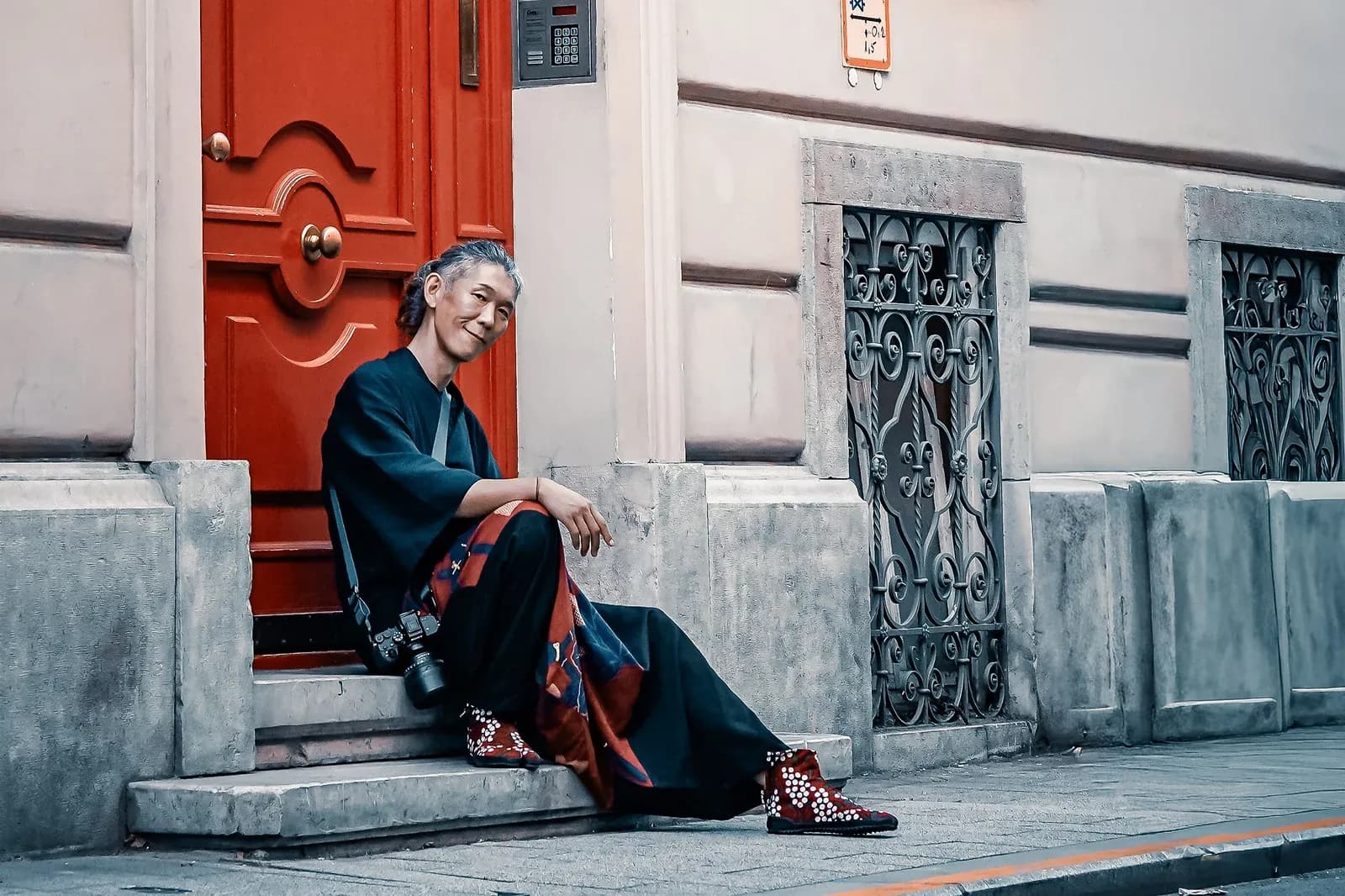 Shintarrow Yoshikawa seated by a red door in Budapest, camera in hand
